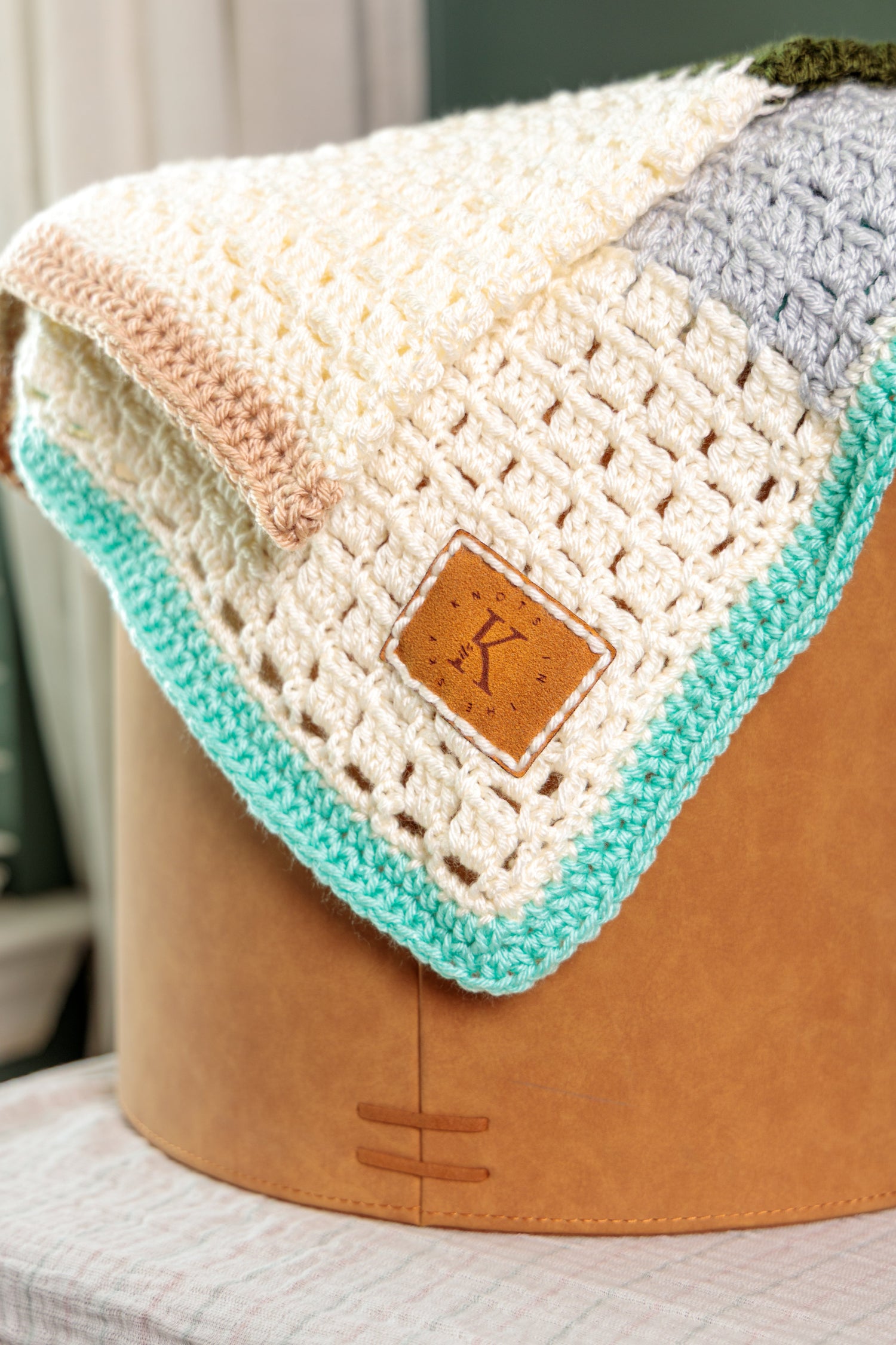 Crocheted baby blanket in cream and mint with a faux suede Knots in the Sky tag.