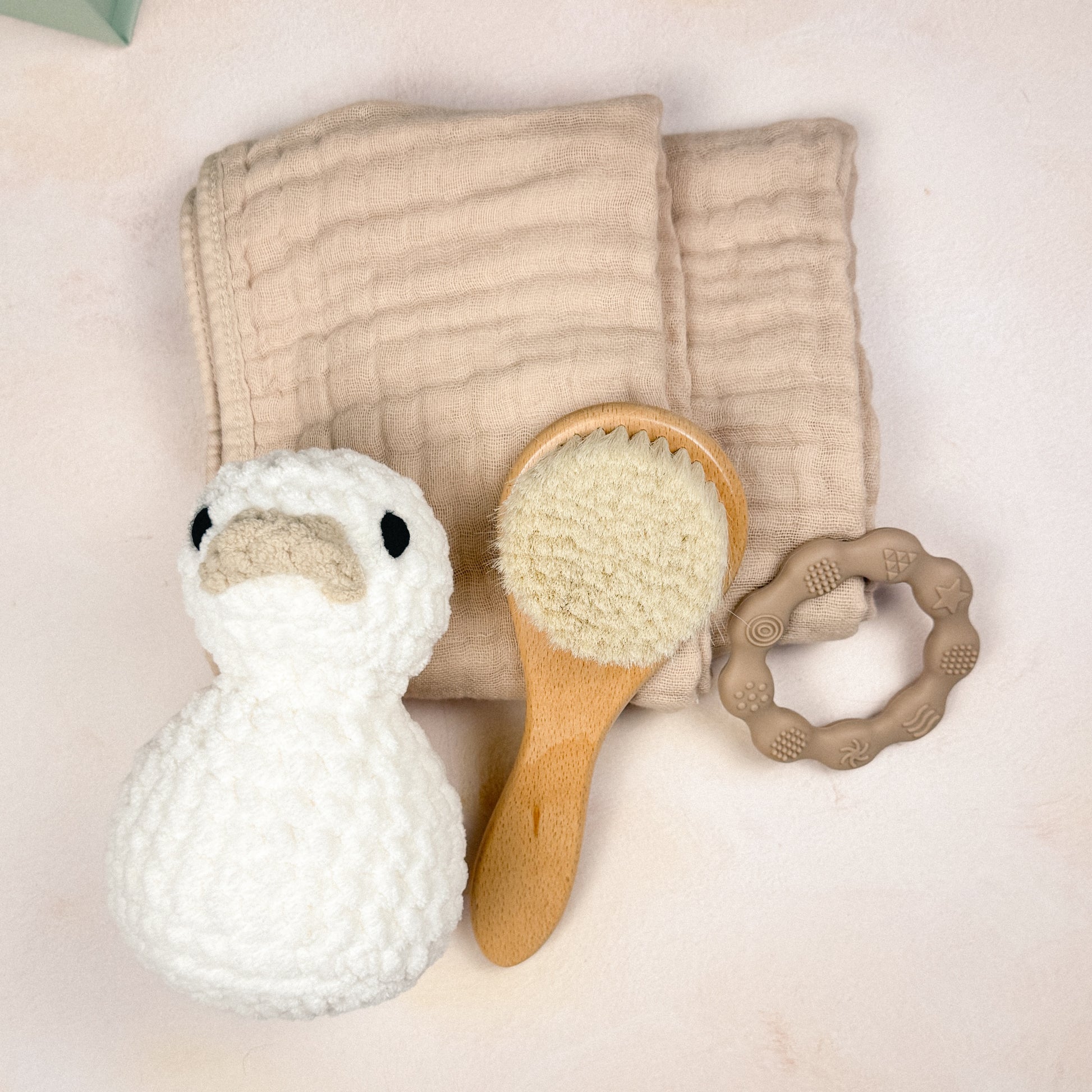Flat lay of the Driftwood First Days Edit featuring a plush duck, muslin burp cloths, wooden baby brush, and silicone teether.