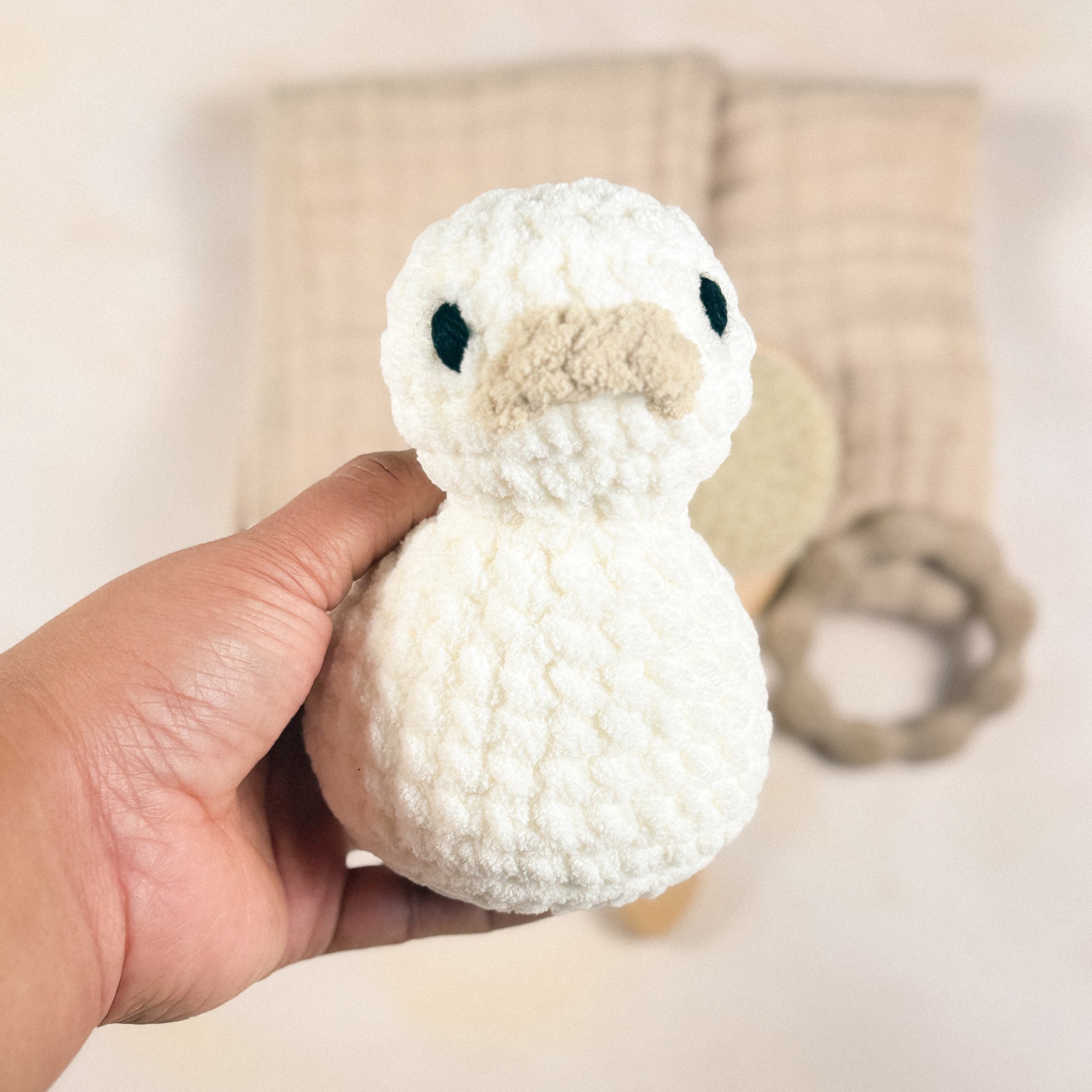 Hand holding the plush duck included in the First Days Edit to show size and scale, with a blurred background