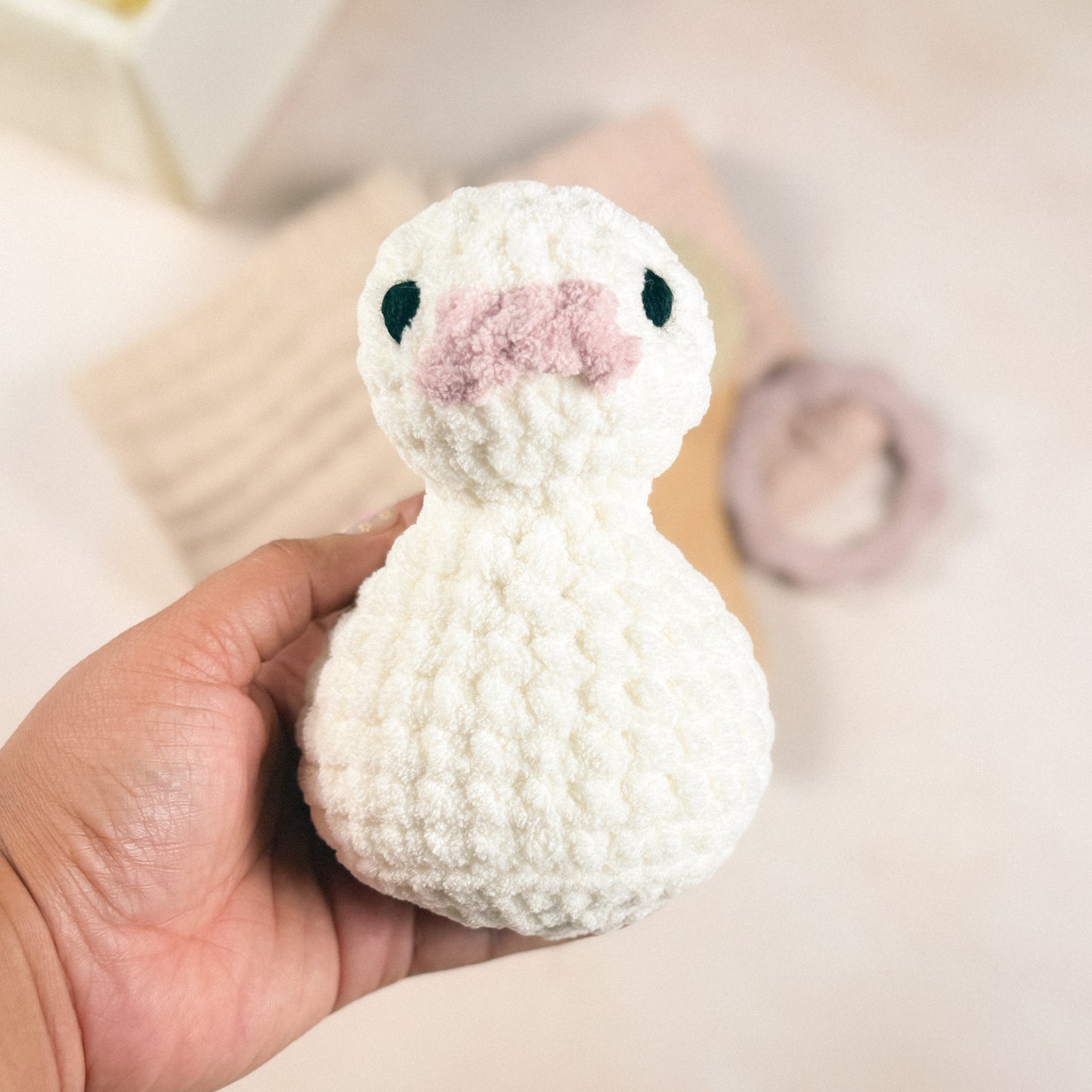 Hand holding the plush duck included in the First Days Edit to show size and scale against a blurred background.
