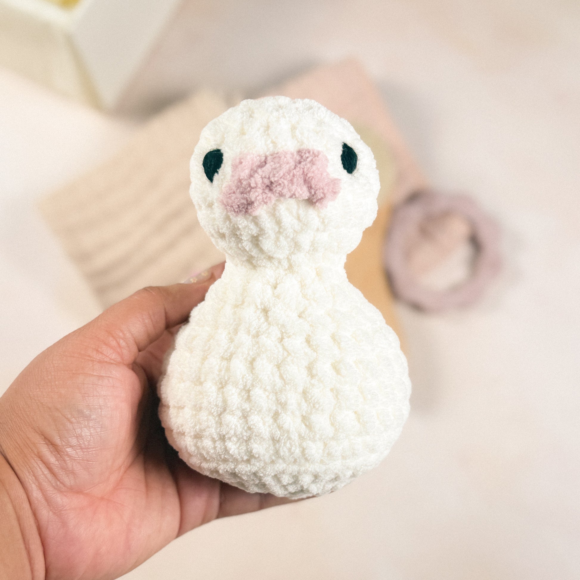 Hand holding the plush duck included in the First Days Edit to show size and scale against a blurred background.