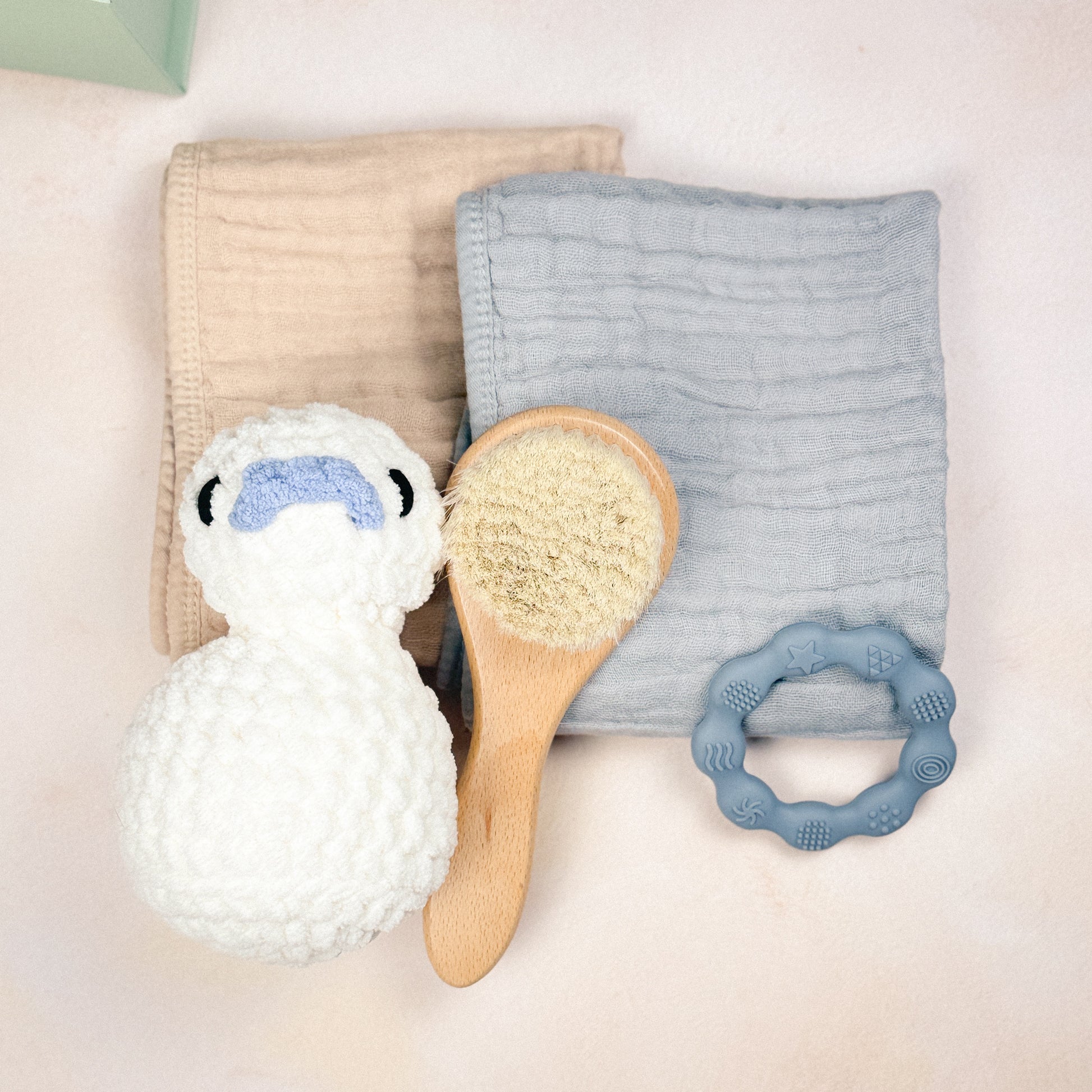 Flat lay of the Stone Blue First Days Edit featuring a plush duck, muslin burp cloths, wooden baby brush, and silicone teether.