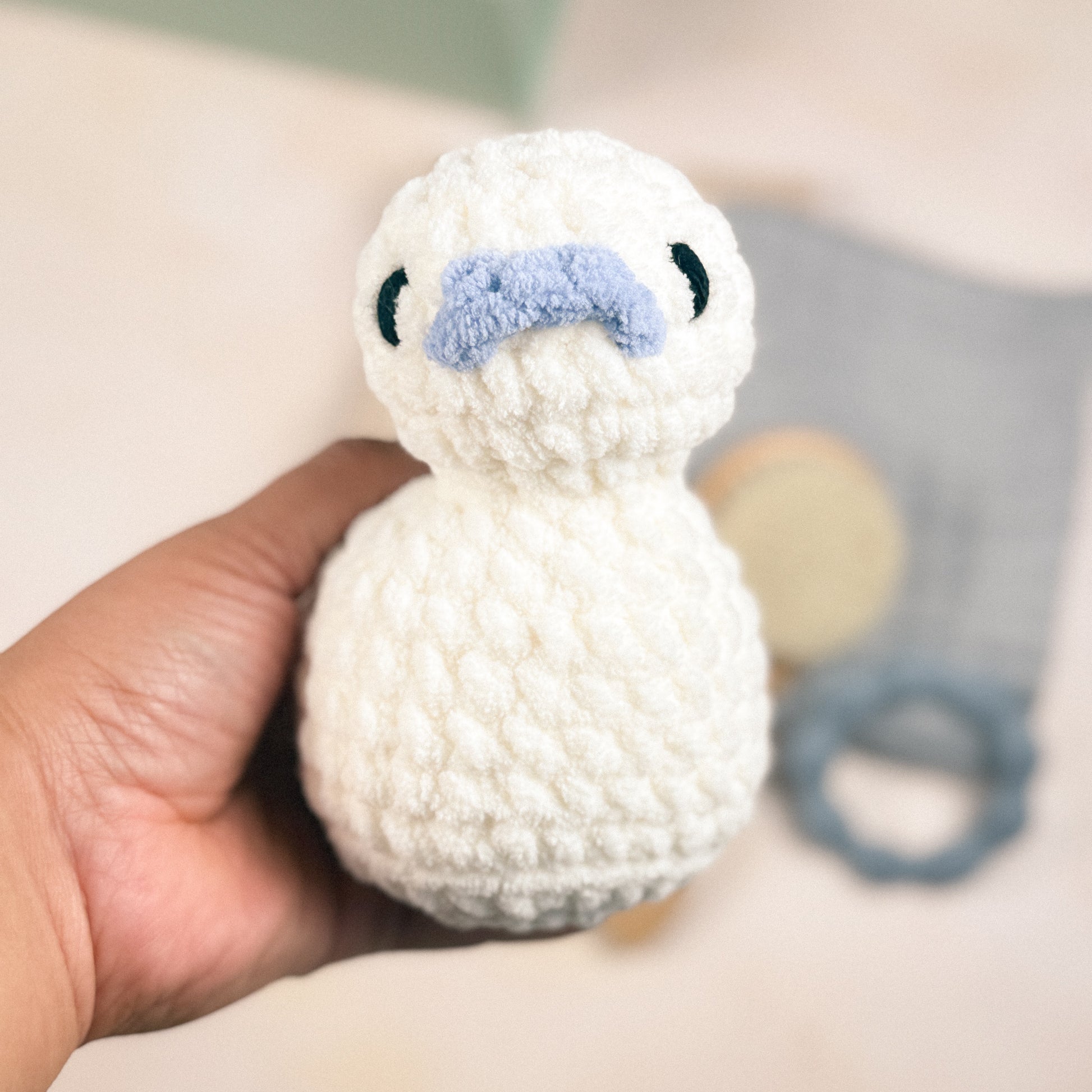 Hand holding the plush duck included in the First Days Edit to show size and scale, with a blurred background
