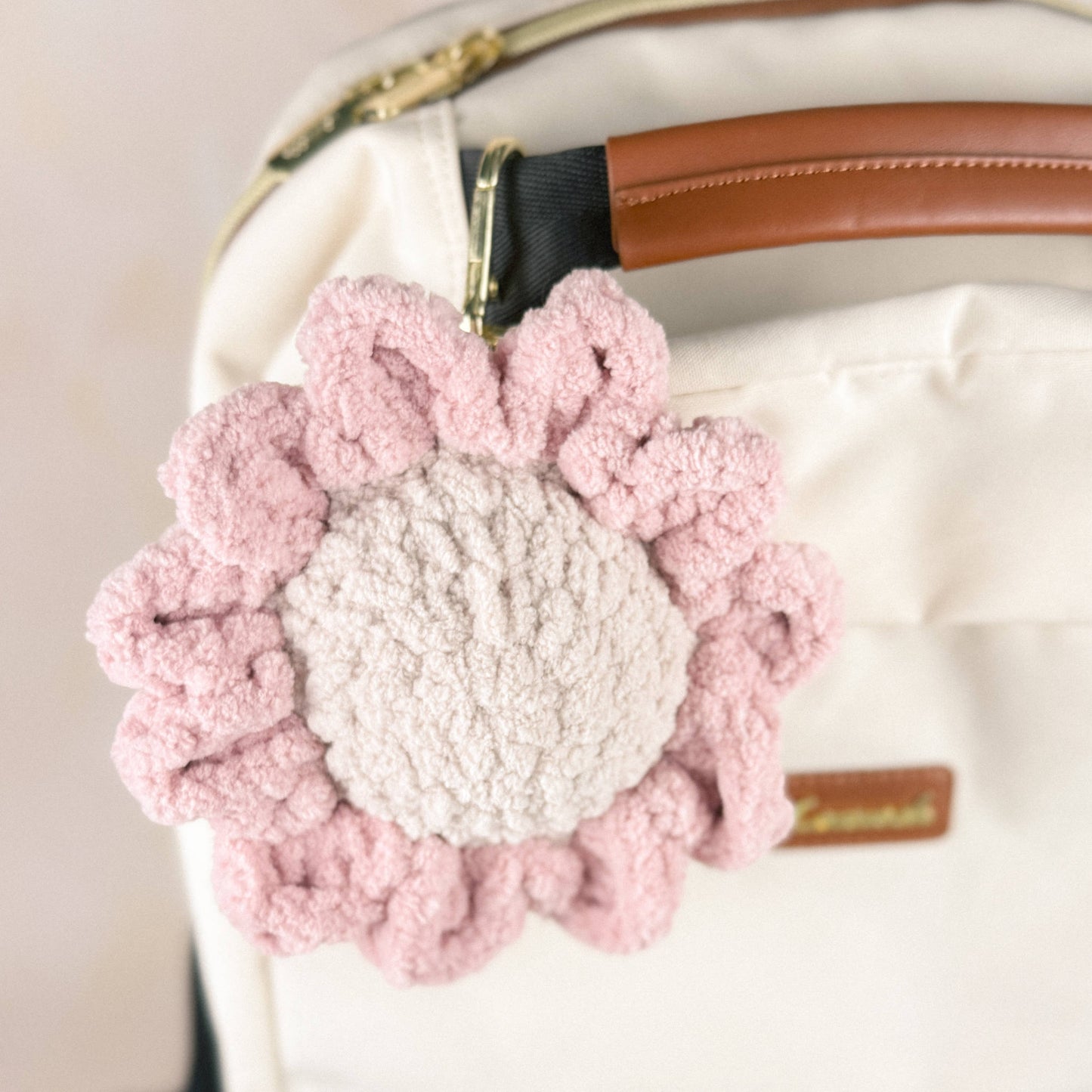 Crochet daisy charm attached to a neutral-colored backpack, shown hanging to display scale and size.