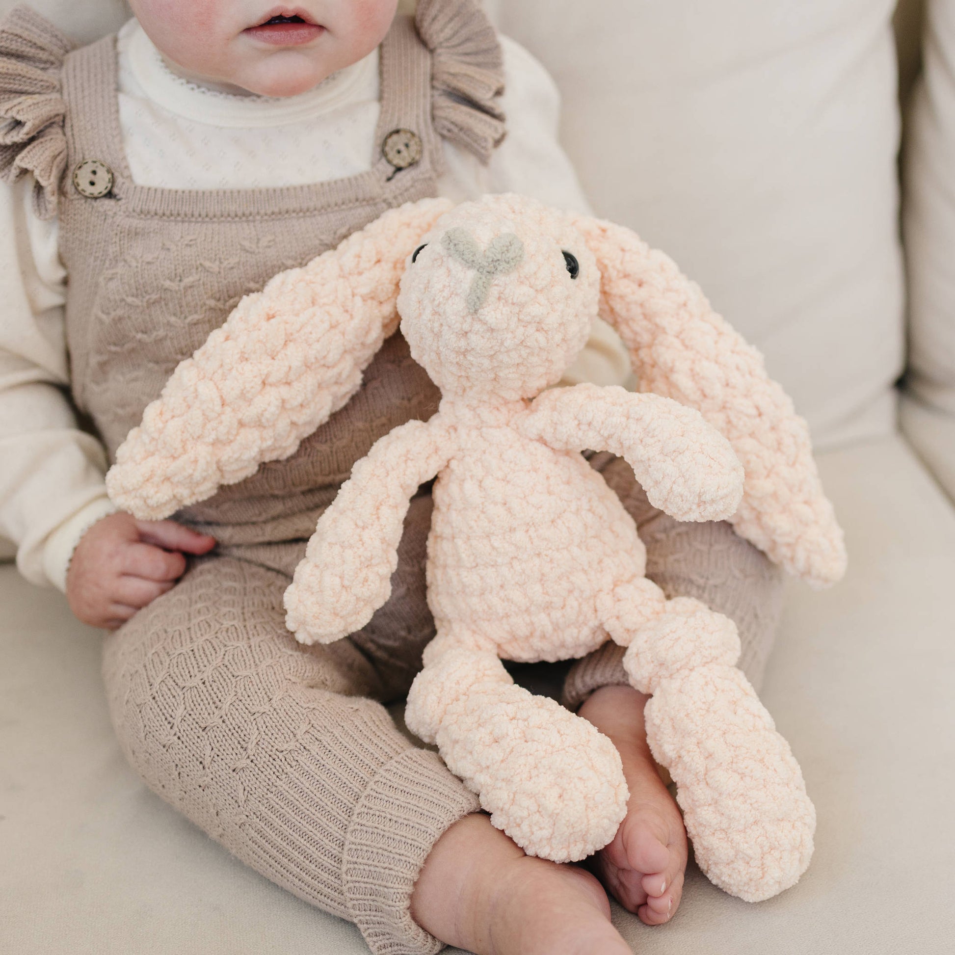 Child holding a plush bunny toy on a light-colored couch to show scale.