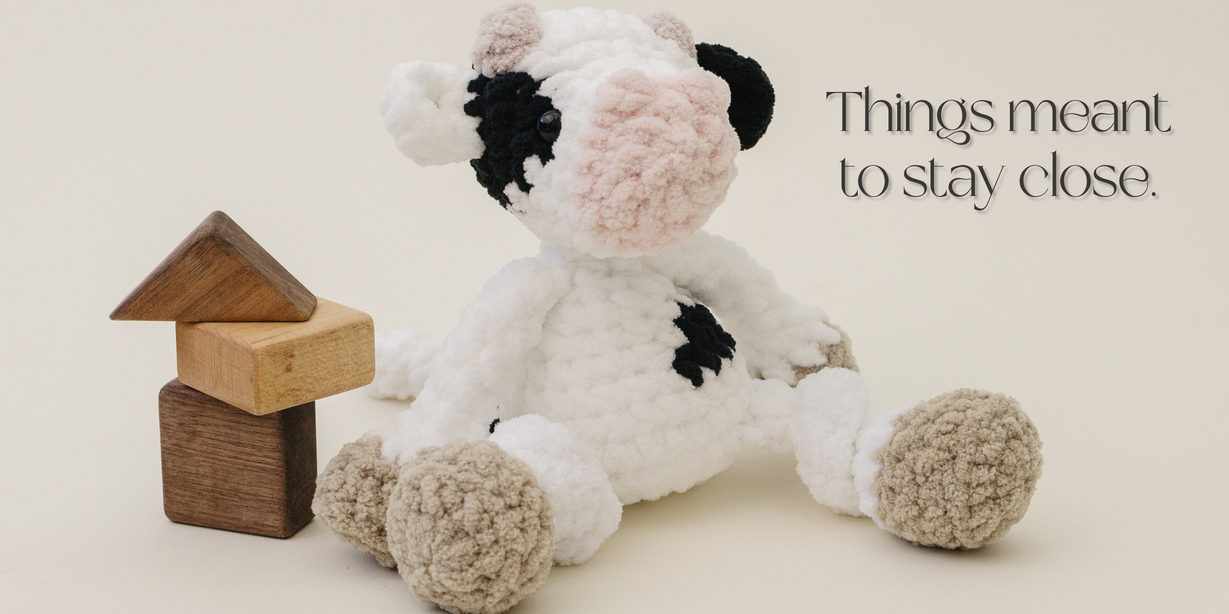 Black and white cow plush seated on a neutral surface beside stacked wooden blocks.