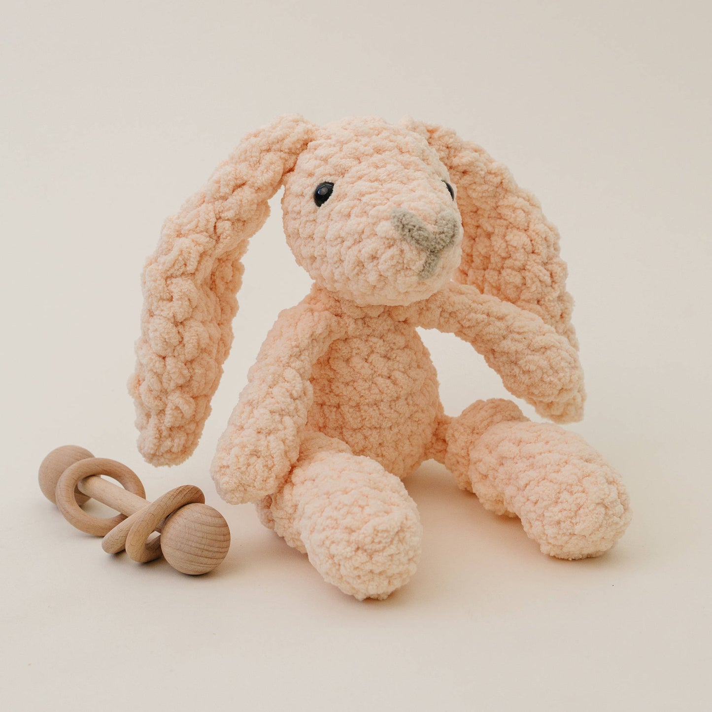 Plush peach bunny toy with wooden rattle on a light background