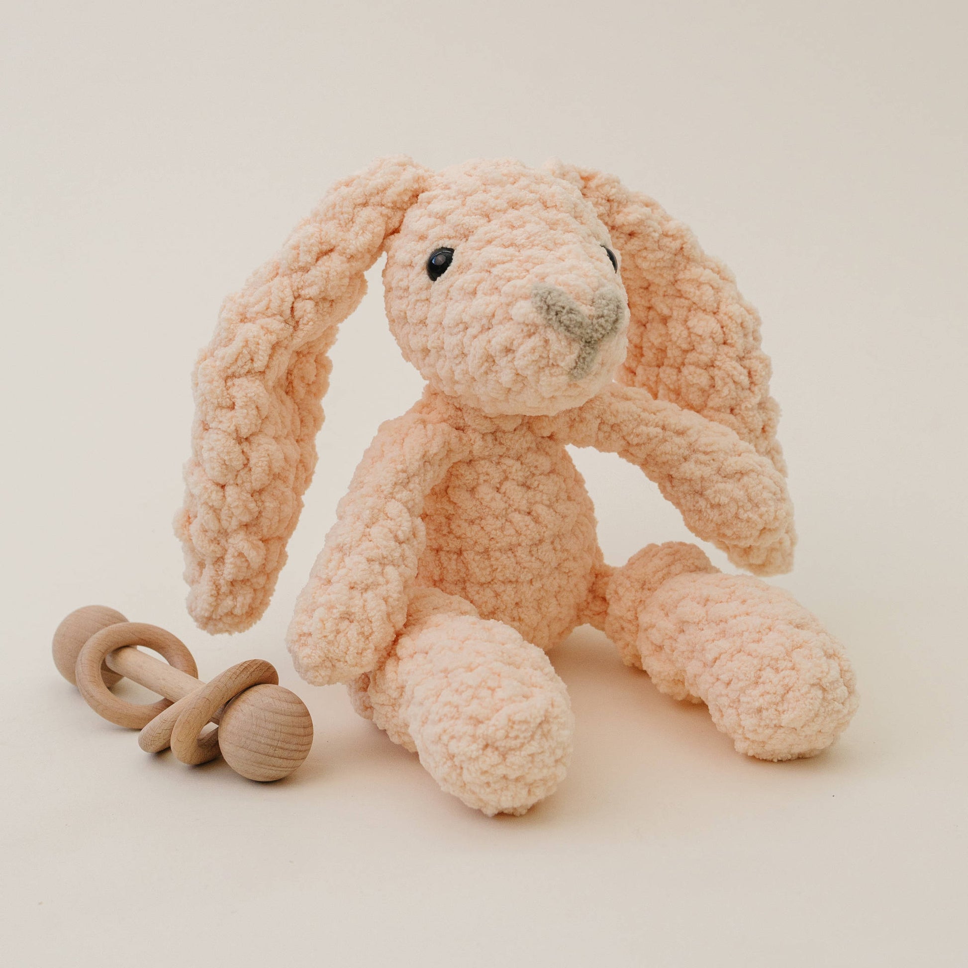 Plush peach bunny toy with wooden rattle on a light background
