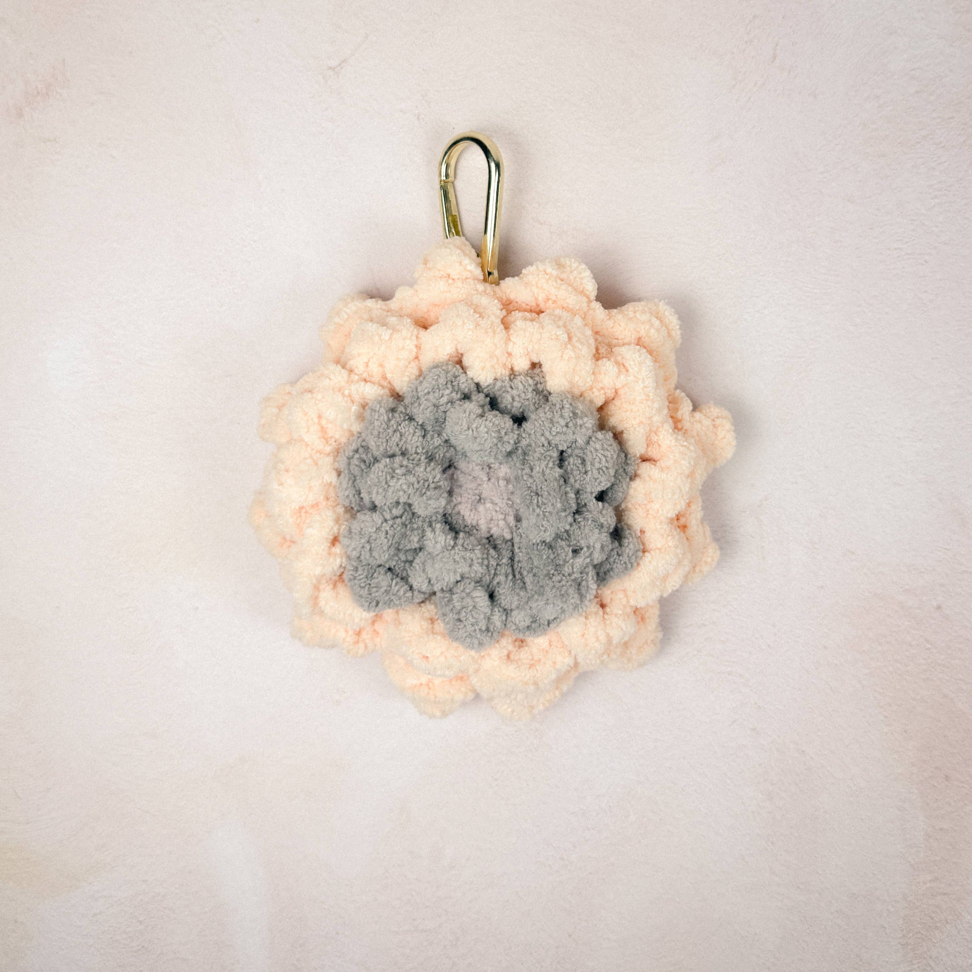 Crochet peach Gerber flower charm laid flat on a neutral background, showing  flower detail.
