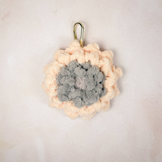 Crochet peach Gerber flower charm laid flat on a neutral background, showing  flower detail.