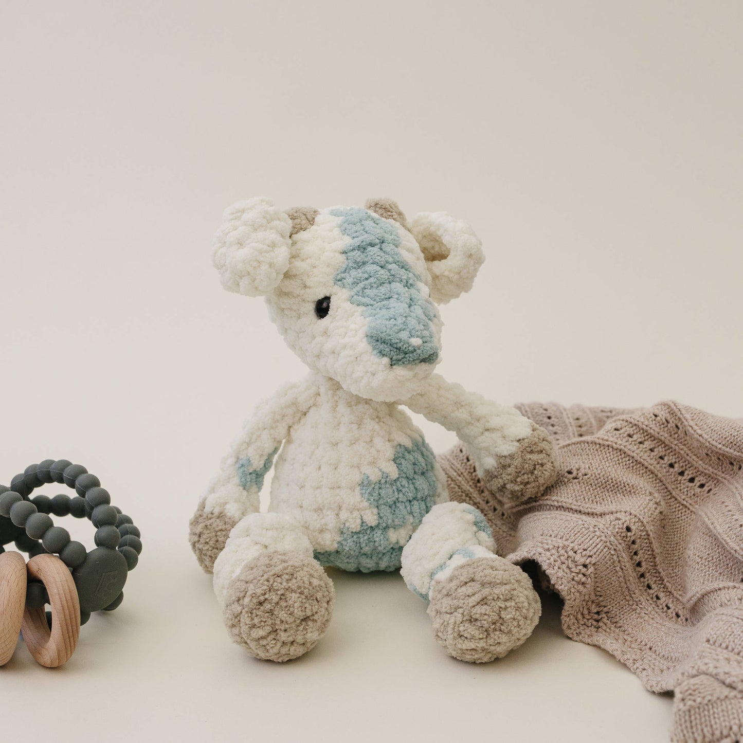 Goat plush shown on a neutral background beside a folded blanket and wooden toy to show scale.