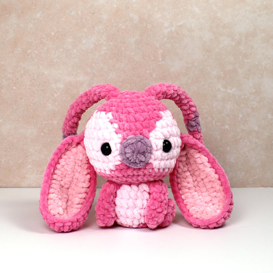 Handmade crochet plush creature in pink with long ears and light pink and purple accents. Handmade toy perfect for unique gifts or collections.
